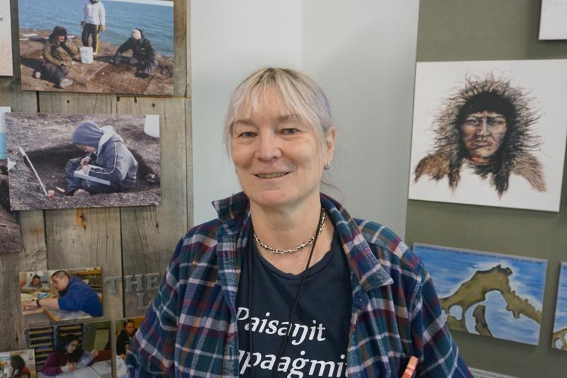 Archaeologist Anne Jensen stands next to a display at the Barrow Arctic Research Center that explains her work rescuing eroding cultural sites in and around Utqiagvik. (Photo by Yereth Rosen/Alaska Beacon)